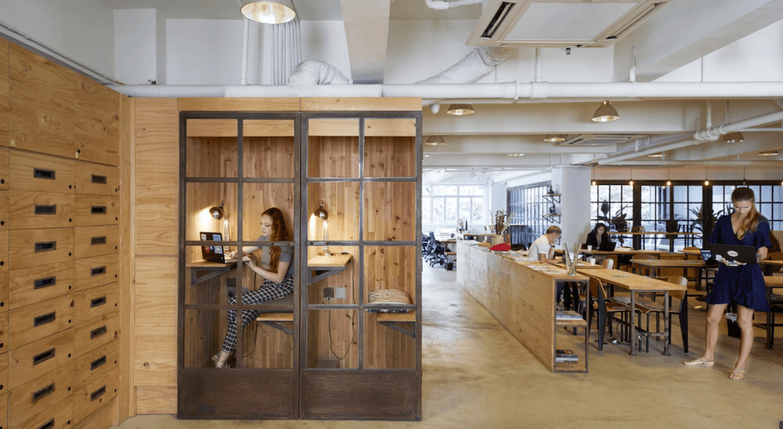 Cozy coworking space with wooden focus pods, communal tables, and people working on laptops