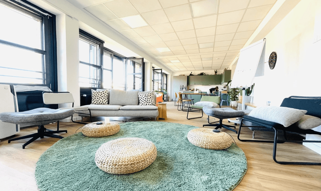 Cozy modern coworking space with comfortable seating, a rug, and a kitchen area in the background.